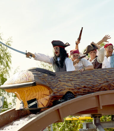 Fyra personer utklädda till pirater åker en stockbana i en nöjespark. De skriker och gestikulerar med svärd och pistoler i luften