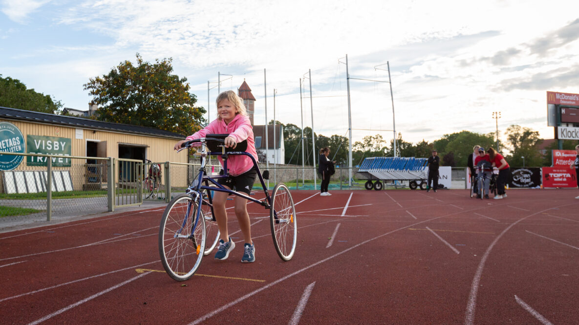 Ca 10-årig tjej med en racerunner-cykel på friidrottsbana utomhus