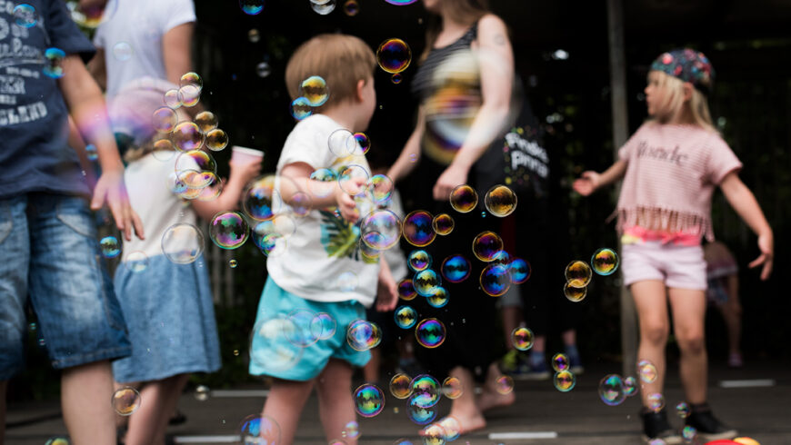 Barn och vuxna leker bland såpbubblor på en utomhusscen