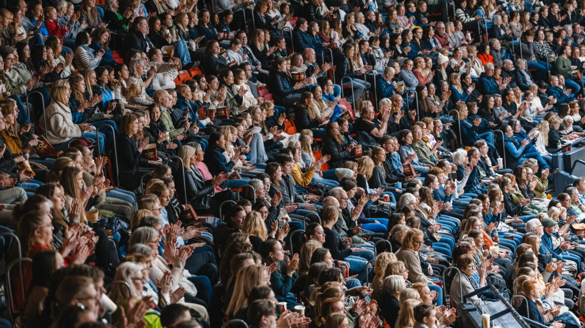 Publik sitter tätt och applåderar på läktare i en arena