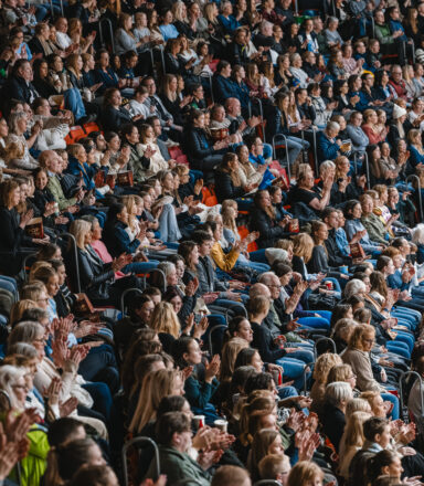 Publik sitter tätt och applåderar på läktare i en arena