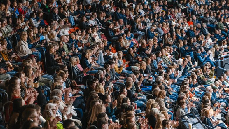 Publik sitter tätt och applåderar på läktare i en arena