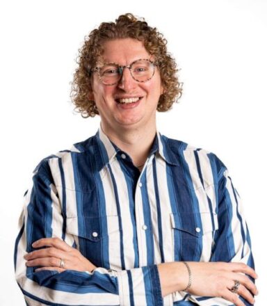 Klaus wearing a blue and white striped shirt and glasses, smiling to the camera